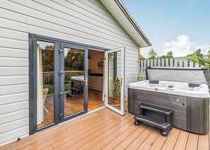 A deck with a hot tub, a sliding glass door leading to a patio, and a small table with chairs.