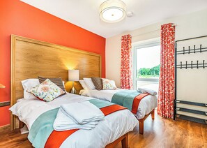 A hotel room with two beds, a wooden headboard, a nightstand with a lamp, a window with curtains, and a coat rack. - 3 bedroom accommodation in Flaxton (Flaxton)