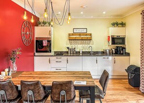 A modern kitchen with a dining area, featuring a wooden table, chairs, and a red accent wall.