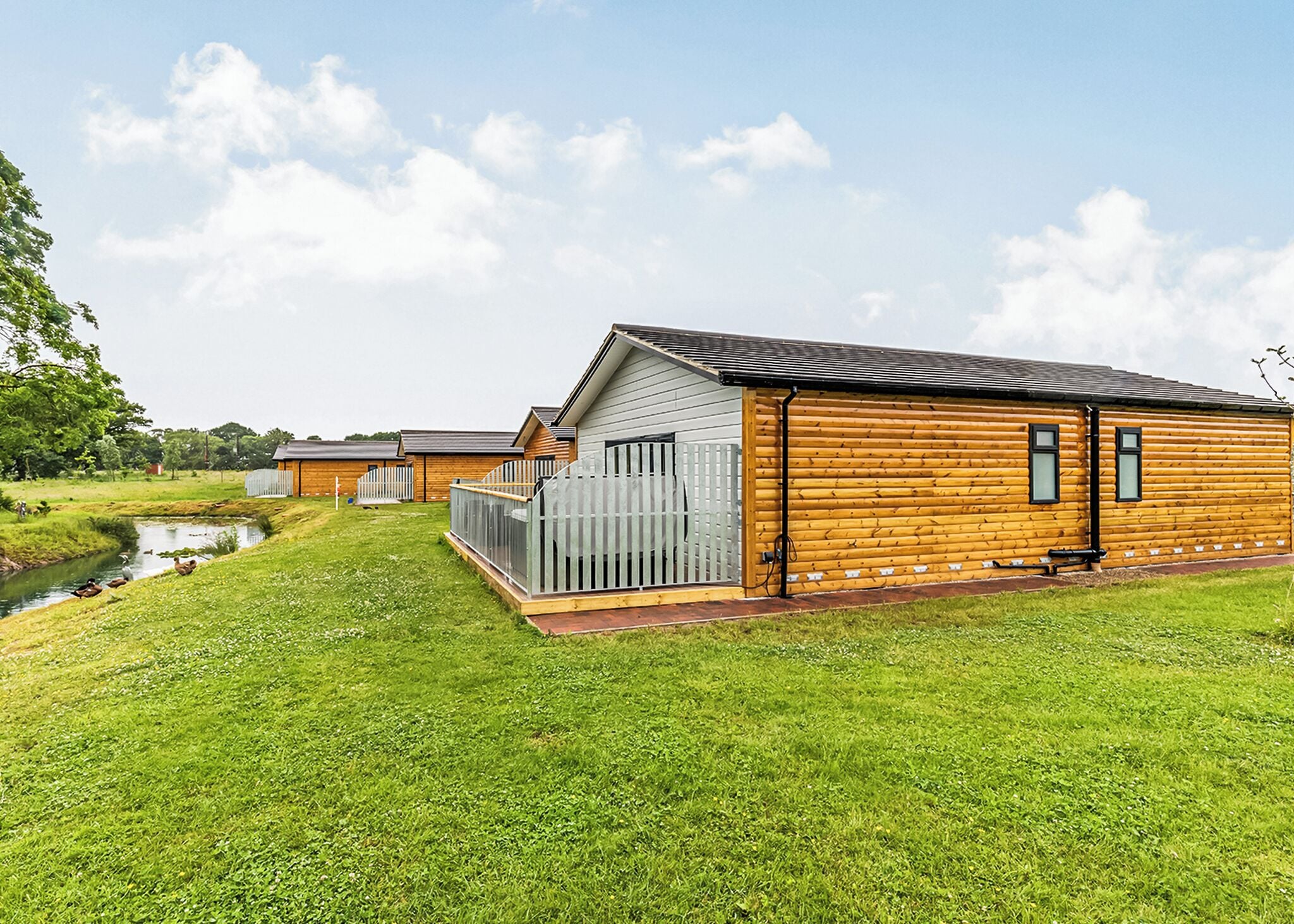 Une rangée de cabanes en bois, avec une pelouse verdoyante et un petit ruisseau.