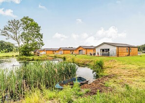 A row of wooden cabins with a pond and a boat in the foreground.