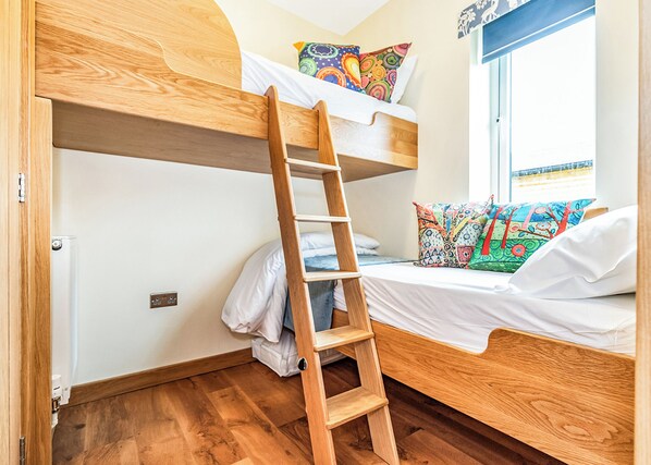 A bunk bed room with a wooden ladder, white bedding, and colorful pillows.