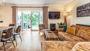 Een woonkamer met een bank, een televisie, een open haard en een eethoek met stoelen en een tafel.