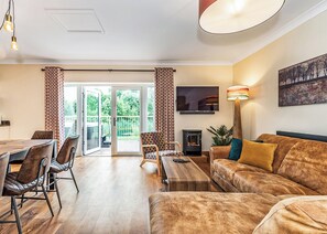 A living room with a sofa, a TV, a fireplace, and a dining area with chairs and a table. - 3 bedroom accommodation in Flaxton (Flaxton)