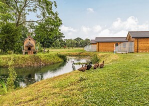 A wooden birdhouse near a pond, a fenced area, and a building with a sloped roof.