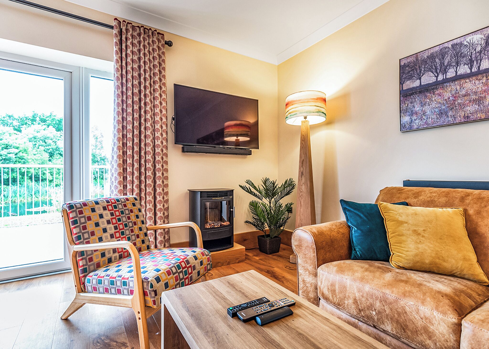 Un salon comprenant un canapé, un fauteuil à motifs, une cheminée, un téléviseur et un lampadaire.