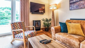 Een woonkamer met een bank, een gestreept fauteuil, een open haard, een televisie en een vloerlamp.