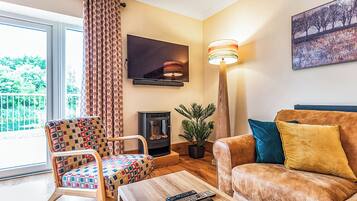 Un salon comprenant un canapé, un fauteuil à motifs, une cheminée, un téléviseur et un lampadaire.