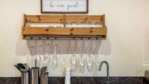 Une cuisine avec un meuble à vin en bois contenant plusieurs verres, un évier et un plan de travail avec des ustensiles de cuisine.