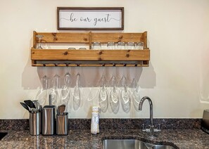 A kitchen with a wooden wine rack holding several glasses, a sink, and a countertop with utensils. - 3 bedroom accommodation in Flaxton (Flaxton)