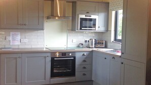 A compact kitchen with a built-in oven, microwave, and stainless steel range hood. - Boutique and spacious luxury lodge, perfect for a romantic escape. (West Tanfield)