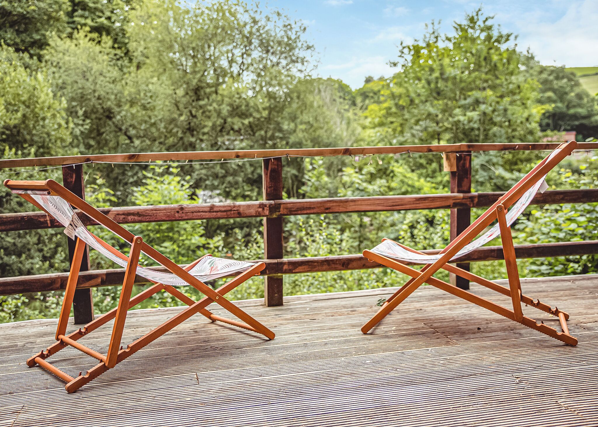 A wooden deck with two wooden chairs and a wooden table.