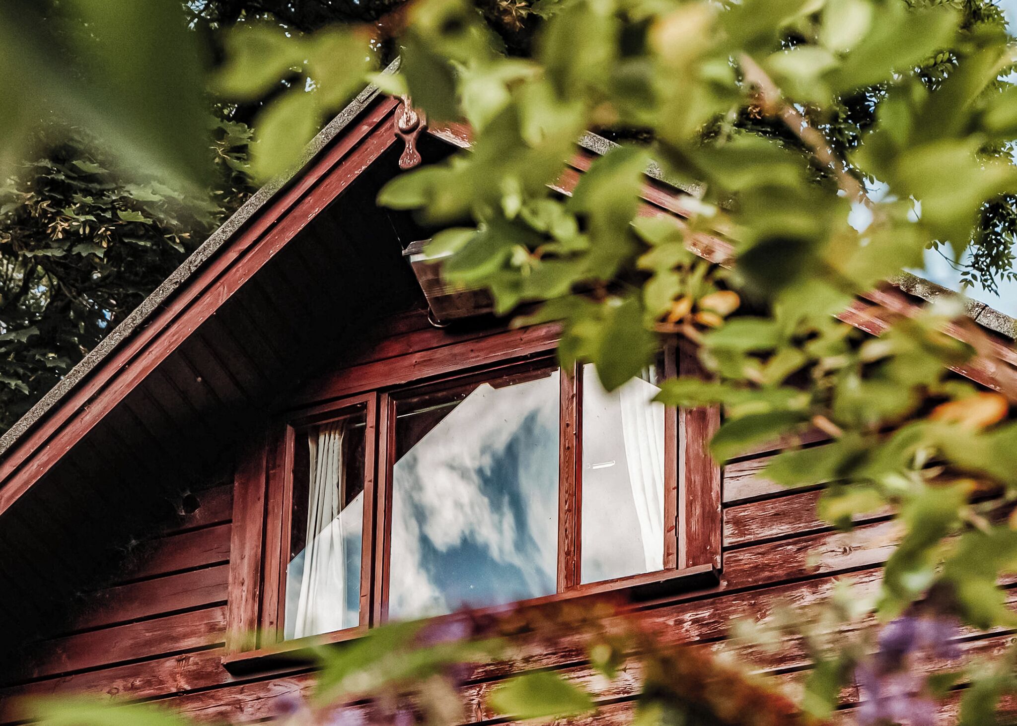 Une cabane en bois rustique, dotée d’un toit en pente, d’une fenêtre avec des rideaux et offrant une vue sur le ciel.