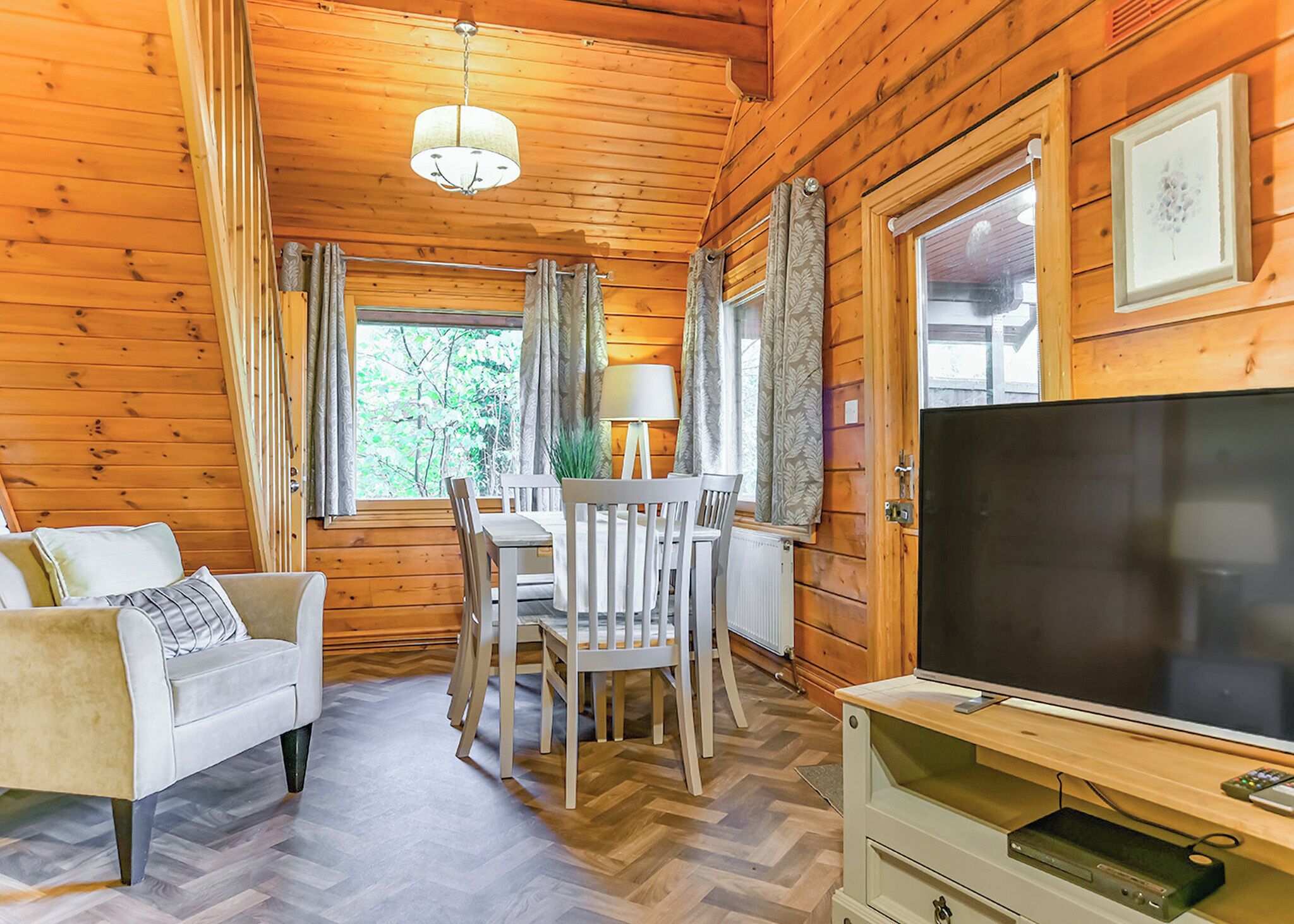 L’intérieur chaleureux d’un chalet avec un canapé, une table à manger, des chaises, un téléviseur et des murs en bois.