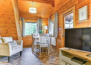 A cozy cabin interior with a sofa, dining table, chairs, a TV, and wooden walls. - 3 bedroom accommodation in Caerwys, Flintshire (Caerwys, Flintshire)