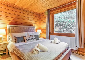 Een slaapkamer in een houten chalet met een bed, kussens, een raam en een nachtkastje.