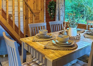 A wooden dining table set with bowls and plates, surrounded by chairs, with a staircase and greenery visible in the background. - 3 bedroom accommodation in Caerwys, Flintshire (Caerwys, Flintshire)