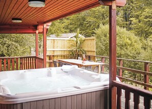 A hot tub on a wooden deck with a table and chairs, surrounded by a wooden fence and trees. - 3 bedroom accommodation in Caerwys, Flintshire (Caerwys, Flintshire)