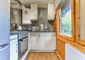 A compact kitchen with white cabinets, a built-in oven, a kettle, and a window with a view of greenery. - 3 bedroom accommodation in Caerwys, Flintshire (Caerwys, Flintshire)