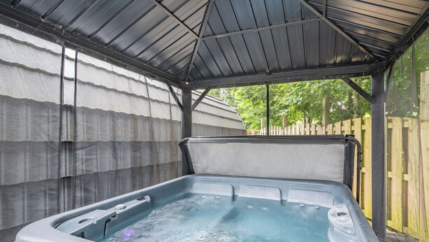 A hot tub under a covered area with a wooden fence in the background.