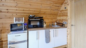 A compact kitchen with a microwave, toaster, and stove, wooden walls, and a white cabinet.