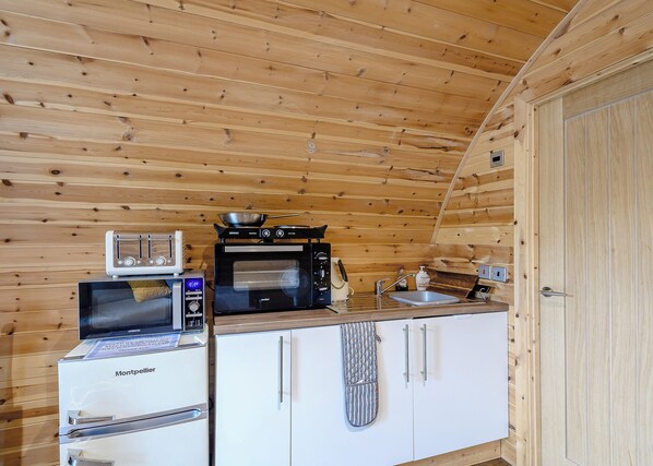 Une cuisine compacte équipée d’un four à micro-ondes, d’un grille-pain et d’une cuisinière, avec des murs en bois et un meuble blanc.