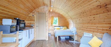 Un intérieur chaleureux, avec des éléments en bois, comprenant un coin cuisine, un lit et un espace salon.