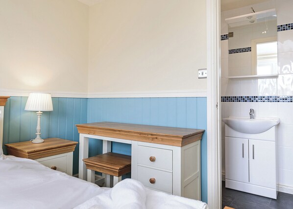 A bedroom with a bed, bedside table, nightstand, dresser, and a bathroom with a sink and mirror.