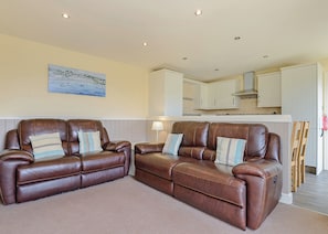 A living room with two leather sofas, a painting on the wall, and a kitchen in the background.