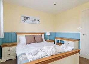 Un lit bien fait, avec des oreillers, une table de chevet sur laquelle se trouve une lampe, et un tableau accroché au mur.