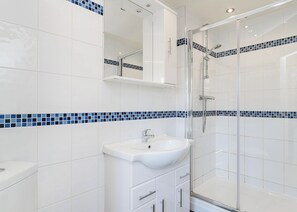Une salle de bain moderne avec des carreaux blancs, une douche en verre et un lavabo blanc.