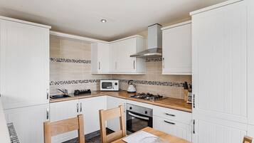 Une cuisine moderne avec des meubles blancs, un four à micro-ondes, une cuisinière à gaz et une table à manger en bois avec des chaises.