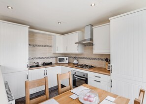 A modern kitchen with white cabinets, a microwave, a gas stove, and a wooden dining table with chairs.