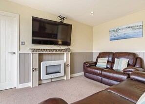 A living room with a flat-screen TV, a fireplace, a brown leather sofa, and a painting on the wall.