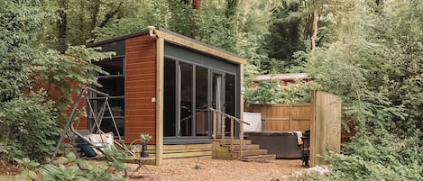 Une petite cabane en bois dotée d’une grande porte-fenêtre coulissante, entourée d’une forêt dense.
