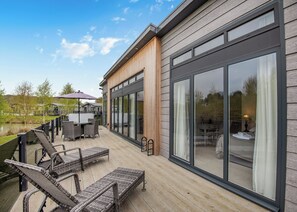 Une terrasse extérieure moderne, dotée de meubles en osier, d’un barbecue et de grandes portes-fenêtres coulissantes.