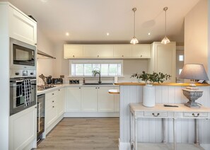 A kitchen with white cabinetry, a built-in oven, a sink, and a window with blinds.