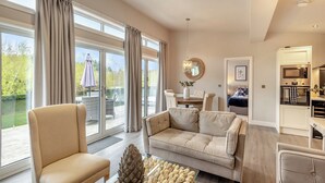 Un salon spacieux avec un canapé, un fauteuil et une table à manger. Il y a un balcon avec vue sur la verdure.