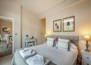 A neatly arranged bedroom with a bed, bedside tables, a desk, and a chair.