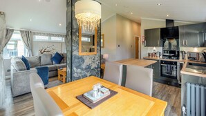 A modern living room with a sofa, a dining table, and a kitchen area with appliances. - New in 2018. Modern and luxurious lodge with lakeside view. (Woodhall Spa)