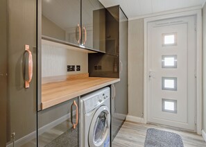 A compact kitchen with a washing machine, a microwave, and a built-in oven. - New in 2018. Modern and luxurious lodge with lakeside view. (Woodhall Spa)
