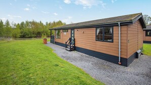 A single-story building with a sloped roof, a small porch, and a gravel driveway. - New in 2018. Modern and luxurious lodge with lakeside view. (Woodhall Spa)