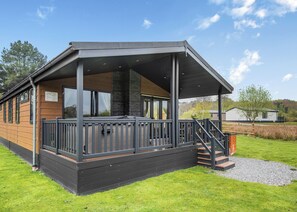 A modern building with a covered porch, a staircase, and a grassy area. - New in 2018. Modern and luxurious lodge with lakeside view. (Woodhall Spa)