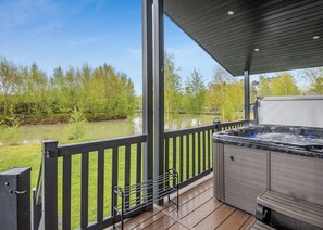 A covered outdoor deck with a hot tub, wooden flooring, and a view of a lake and trees. - New in 2018. Modern and luxurious lodge with lakeside view. (Woodhall Spa)