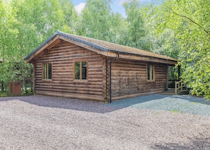 A log cabin with a gravel driveway and a wooden porch.