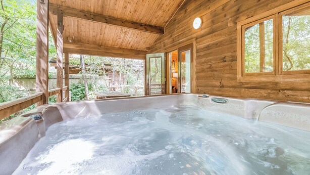 A wooden cabin with a hot tub, large windows, and a view of the surrounding forest. - 2 bedroom accommodation in Freehay, Cheadle (Freehay, Cheadle)