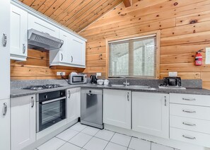 Une cuisine moderne avec des meubles blancs, une cuisinière à gaz, un lave-vaisselle et une fenêtre équipée de stores.