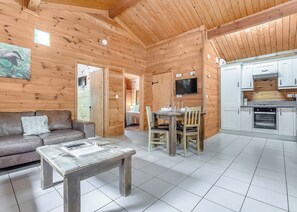 Een houten cabin met een bank, eettafel, stoelen, een televisie en een keukenhoek.