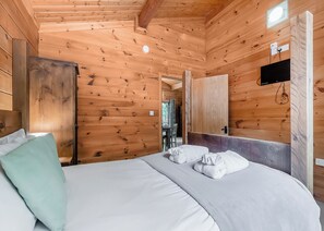 Une chambre rustique en bois, avec un lit, un bureau et un téléviseur fixé au mur.