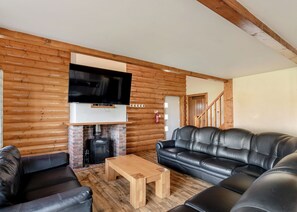 Interior d'una cabana de fusta amb una xemeneia, sofàs de cuir, una taula de centre de fusta i un televisor penjat.